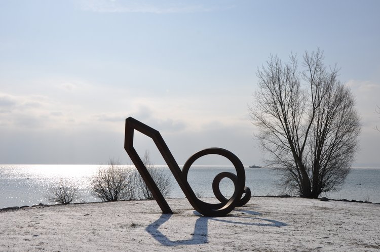 Moderne Skulptur am winterlichen Ufer beim Hotel Traube am See mit kahlem Baum und Bodenseehintergrund.